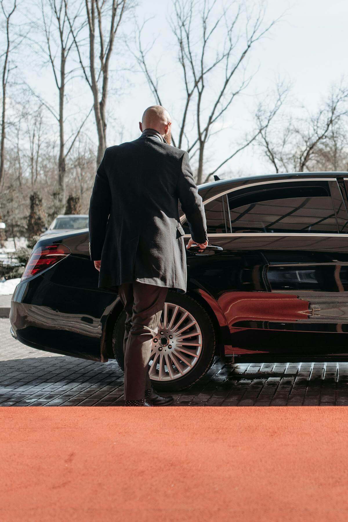 Chauffeur in a suit approaching a luxury car on a sunny day