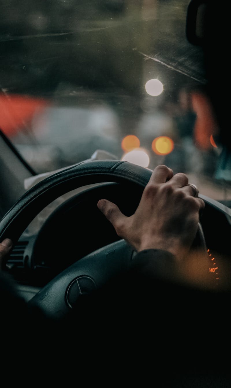 Hand on a steering wheel at night driving through city lights